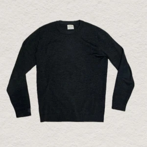 Mörkgrå stickad tröja från A Days March  - En stilren mörkgrå stickad tröja från A Days March i mjuk ullblandning. Tröjan har rund halsringning, långa ärmar och ribbade muddar vid ärmslut och nederkant. Perfekt basplagg för lager på lager och enkel att matcha. Har dock en litet hål vid ryggen men ytterst litet och går att fixa enkelt. Skriv gärna vid frågor!