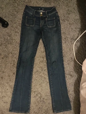 Madlady bootcut jeans TALL💌 - Snygga mörkblå bootcut-jeans från Madlady med fickor baktill och en superfin passform. 💕Perfekta för dig som är längre, då modellen är TALL och sitter riktigt bra på långa ben💌  ❣️Bootcut-modell ❣️ Mörkblå färg – lätt att matcha ❣️ Fickor baktill ❣️Storlek 34, TALL  ⚠️ Finns slitningar längst ner på benen, men inget som påverkar användningen – i övrigt är jeansen i bra skick och fortfarande mycket snygga.Innerbenslängden 90 cm & midjemått 32 cm💕