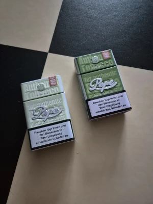 Metallburkar Pepe grön - Två små metallburkar från Pepe i grön färg med vit och silverfärgad logga. Burkarna har rektangulär form och lock som går att öppna och stänga. Perfekta för att förvara småsaker eller som dekoration.