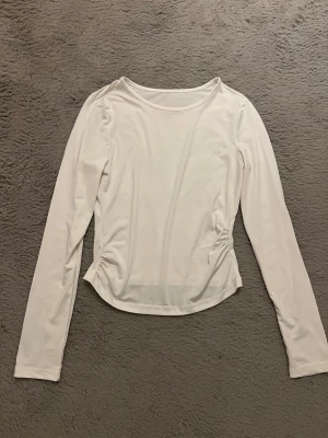 Vit långärmad topp med rund hals - En stilren vit långärmad topp med rund halsringning och lätt figurnära passform. Perfekt att matcha med jeans eller kjol för en clean look. Tillverkad i mjukt material som känns skönt mot huden.