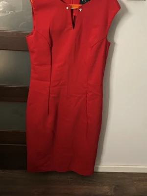 Röd figurnära klänning med diamantdetalj - Snygg röd klänning från Mohito i figurnära modell. Klänningen är ärmlös och har en dekorativ pärldetalj vid halsringningen samt en liten slits framtill. Perfekt för dig som vill sticka ut med en klassisk men trendig look.