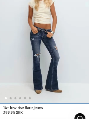 Mörkblå low rise flare jeans - Säljer ett par mörkblå low rise flare jeans med slitningar och hål på benen. Jeansen har utsvängda ben, kontrastsömmar och broderade bakfickor. Perfekta för en trendig och avslappnad look.