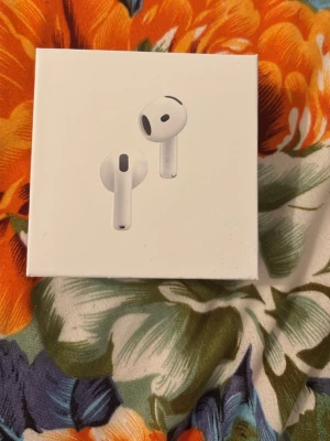 Apple AirPods 4 trådlösa hörlurar - Säljer ett par vita Apple AirPods 4 med stilren och kompakt design. Hörlurarna är trådlösa och har en rundad form i plast, perfekt för dig som vill ha smidiga och snygga hörlurar till mobilen eller datorn.
