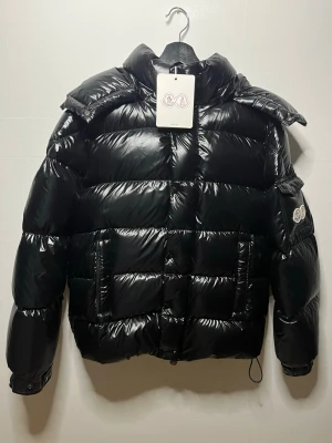 Moncler jacka svart - Svart Moncler jacka i ny skick förutom att där man justerar är syd ihop men inget som syns, den har NFC i loggan, storleken är 4 som motsvarar L, pm vid frågor eller detaljbilder och kom gärna med prisförslag.