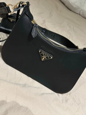 Svart axelremsväska  - Snygg svart handväska  i klassisk modell med guldfärgade detaljer och dragkedja.