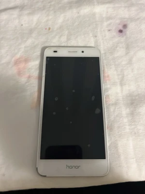 Honor mobiltelefon silvervit - Snygg Honor-smartphone i silver med vit framsida. Telefonen är trasig och fungerar inte helt som den ska, men det är möjligt att vissa delar fortfarande fungerar. Säljs i befintligt skick – kan passa för reparation eller reservdelar.