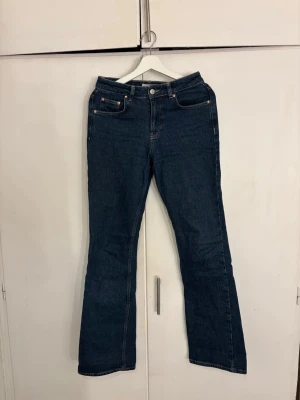 Mörkblå bootcut jeans - Säljer ett par mörkblå bootcut jeans med klassisk femficksdesign och hög midja. Jeansen har raka ben som går ut lite nedtill och är sydda i ett kraftigt denimtyg. Perfekta för dig som gillar en tidlös och avslappnad stil.