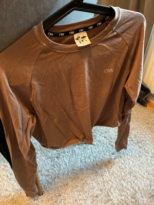 Brun långärmad tröja från ICANIWILL - Långärmad brun träningströja från ICANIWILL med rund hals och diskret logga på bröstet. Tillverkad i ett mjukt och stretchigt material som passar perfekt till gymmet eller löprundan. Nästan aldrig använd och normal k storleken.