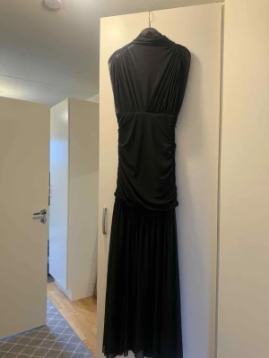 Svart långklänning med meshdetaljer - Säljer en svart långklänning från Zara med transparent mesh upptill och draperade detaljer. Klänningen har en elegant, figurnära passform och är ärmlös. Perfekt för dig som vill ha en stilren och sofistikerad look.