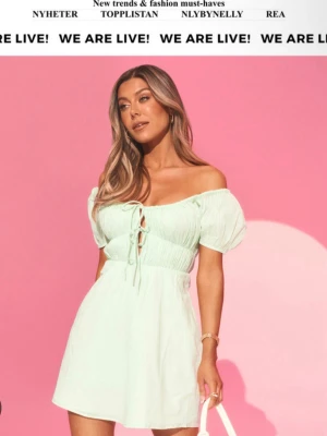 Ljusgrön offshoulder klänning med snörning - Bianca x Nelly. Söt ljusgrön kortklänning med offshoulder och puffärmar. Klänningen har snörning framtill och markerad midja för en feminin siluett.