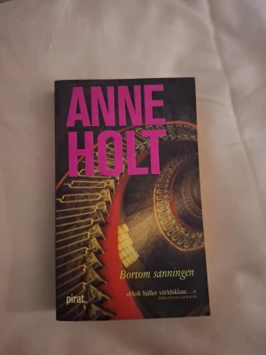 Bortom sanningen av Anne Holt - En spännande kriminalroman av Anne Holt, med svart omslag och stora rosa bokstäver. Boken handlar om kriminalkommissarie Hanne Wilhelmsen och ett brutalt mordfall i Oslo. Pocketutgåva, tryckt på papper.