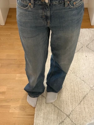 Blå raka jeans  - Säljer ett par klassiska blå jeans med rak passform. Jeansen har fem fickor, knappgylf och subtila slitningar för en avslappnad look. Perfekta till en enkel topp eller hoodie. Materialet är kraftig denim i bomull.