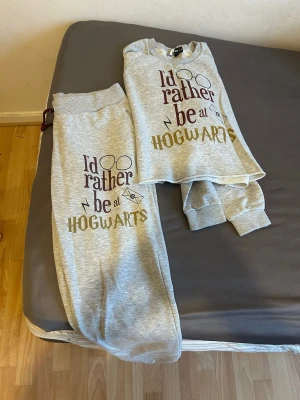 Grå Harry Potter pyjamas-set - Mysig grå pyjamas med trycket 'I'd rather be at Hogwarts' och Harry Potter-inspirerade detaljer som glasögon, blixt och brev. Setet består av långärmad tröja och byxor med resår i midjan och mudd vid benslut. Perfekt för alla Potterheads som vill chilla hemma.