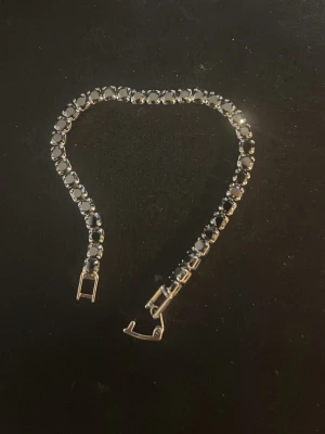 Silverfärgat armband med svarta pärlor - Snyggt armband i silverfärg med runda svarta pärlor längs hela bandet. Armbandet har en klassisk och stilren design med ett smidigt spänne. Perfekt accessoar för dig som gillar en elegant och enkel look.