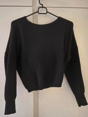 Svart ribbstickad tröja med omlott - Säljer en svart ribbstickad tröja med omlottdetalj i ryggen. Tröjan har lång ärm, rund halsringning och är gjord i ett mjukt, stretchigt material. Perfekt för dig som gillar en enkel men ändå unik look.