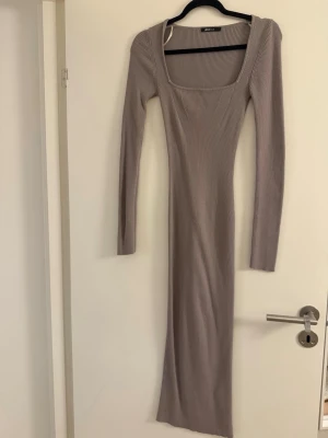 Lång ribbad beige klänning Gina Tricot - Supersnygg långklänning från Gina Tricot i ribbad beige trikå. Klänningen har lång ärm, fyrkantig ringning och sitter tight för en smickrande siluett. Perfekt för dig som gillar minimalistisk och trendig stil.