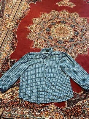 Blå mönstrad skjorta med knappar - Snygg blå skjorta med småmönstrat tryck och klassisk krage. Skjortan har långa ärmar och knäppning framtill. Perfekt för dig som gillar en stilren men ändå unik look.