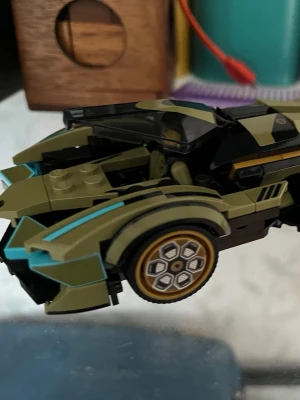 Grön LEGO-bil med gulddetaljer - Säljer en cool LEGO-bil i militärgrönt med svarta och turkosa detaljer. Bilen har guldfärgade fälgar och en genomskinlig svart vindruta. Designen är sportig och futuristisk, perfekt för dig som gillar att bygga och samla LEGO-bilar.
