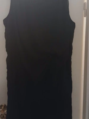 Svart ärmlös kortklänning - En enkel och stilren svart klänning utan ärmar. Klänningen har en rak passform och är knälång, perfekt för dig som gillar minimalistisk stil. Passar till många olika tillfällen och är lätt att matcha med accessoarer.