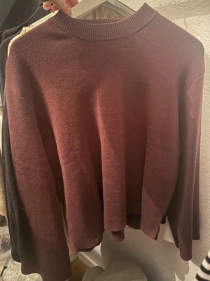 Mörkröd stickad tröja från H&M - En enkel och stilren mörkröd stickad tröja från H&M. Tröjan har rund halsringning, långa ärmar och en rak passform. Perfekt att matcha med jeans eller kjol för en avslappnad look.