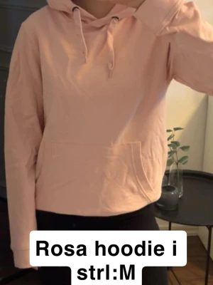 Ljusrosa hoodie med huva - Säljer en ljusrosa hoodie med klassisk huva och dragsnören. Hoodien har en stor magficka framtill och ribbade muddar vid ärmslut och nederkant. Materialet är mjukt och bekvämt och fin färg. Strl m