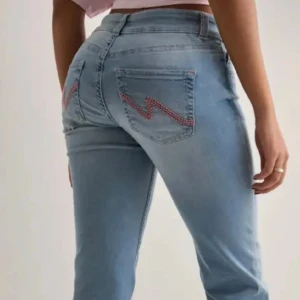 Ljusblå jeans med broderade fickor -  DET ÄR DEM MED HÅL Säljer ett par ljusblå jeans med snyggt rosa broderi i zigzag på bakfickorna. Jeansen har klassisk femficksmodell och sitter tajt över höfterna. Perfekta för dig som vill ha en cool och unik detalj på dina jeans. Low waist, säljer då jag tröttnat, en av tygflärparna där man kan sätta in ett skärp har lostnat men har försökt sytt ihop det så inget som syns 💓