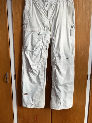 Vita täckbyxor från Peak Performance - Säljer ett par vita täckbyxor från Peak Performance med flera dragkedjeförsedda fickor och detaljer. Tillverkade i slitstarkt Gore-Tex-material som står emot både vind och vatten. Perfekta för vinterns alla äventyr i backen eller på fjället.