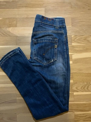 Dondup jeans  - Säljer ett par mörkblå jeans med raka ben och coola slitningar. Jeansen har klassisk femficksdesign, kontrastsömmar och dragkedjegylf. Perfekta för en avslappnad och trendig look. 