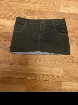 Mönstrad jeanskjol från BDG - Säljer en grön ish kort jeanskjol från BDG med rå kant nertill och kontrastsömmar i gult. Kjolen har klassisk femficksdesign och knappstängning fram. Perfekt för dig som gillar en edgy och avslappnad stil. 