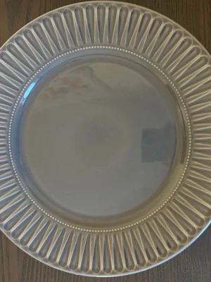 4 st gråa mönstrade tallrikar  - Fyra stycken runda tallrikar i grå färg. Tallrikarna har en dekorativ kant med ett räfflat mönster. Obs!! En tallrik är kantstött, samt om man kollar närmre så är alla tallrikar ”krackelerade”, men inte spruckna. Inget som ses på vanligt håll som man ser på bild 1 där det ej syns!