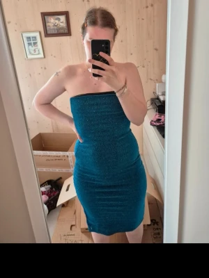 Blå glittrig klänning Gina Tricot - Säljer en blå glittrig klänning från Gina Tricot. Klänningen är tight och axelbandslös med en snygg, kroppsnära passform. Perfekt för dig som vill sticka ut med lite extra glitter.