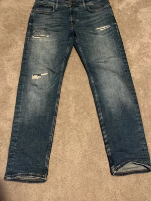 Blå slitna jeans med raka ben - Säljer ett par blå jeans med raka ben och slitna detaljer på framsidan. Storlek 33/30 modell Mike 