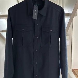 Ny Mörkblå overshirt från Riley, S - Stilren mörkblå overshirt från Riley med klassisk krage, två stora bröstfickor med lock och knappar framtill. Skjortan har lång ärm och är tillverkad i ett mjukt material som känns lyxigt. Perfekt lager-på-lager-plagg för en clean look.