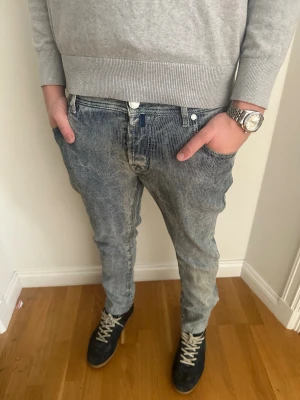 Grå tvättade jeans från Jacob Cohen - Säljer ett par grå tvättade jeans från Jacob Cohen med avslappnad passform och klassisk femficksdesign. Jeansen har tydliga slitningar och vita kontrastsömmar, samt patch med logga bak i midjan. Perfekta för en cool och avslappnad stil.