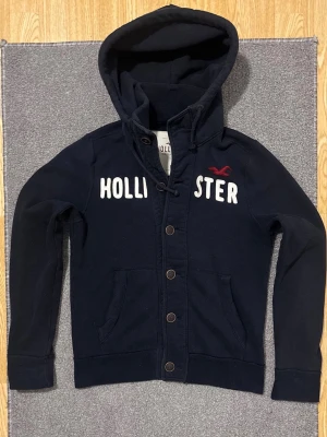 Vintage Hollister Cardigan Med Knappar - Väldigt sällsynt och vintage Hollister hoodie med knappar | Tröjan är i väldigt bra skick utan defekter! | Längd ≈ 63cm, Bredd armhåla-amrhåla ≈ 53cm | Modell 175cm, 68kg | Hör av vid ytterligare frågor och priset kan diskuteras vid snabbt köp! |