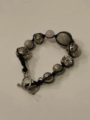Knutet armband med metall och silverfärgade pärlor - Handgjort armband med T-lås gjord av textilsnöre, metallpärlor, glitter/strukturpärlor.
