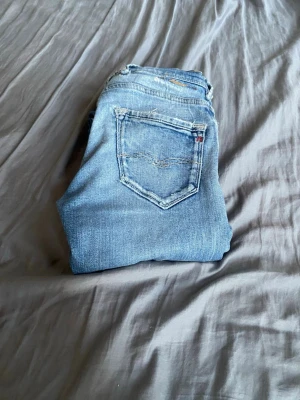 Ljusblå raka jeans från replay - Säljer ett par klassiska ljusblå jeans från replay  med raka ben och femficksmodell. Jeansen har slitna detaljer och den ikoniska röda Levi's-lappen på bakfickan. Perfekta till en avslappnad stil och tillverkade i mjuk denim.