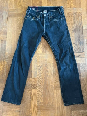 Svarta jeans från True Religion - Snygga svarta jeans från True Religion med raka ben och kontrastsömmar. Klassisk femficksmodell och ikoniska broderade bakfickor. W31