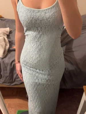 Ljusblå spetsklänning med smala band - Säljer en lång, ljusblå klänning med smala axelband och vacker spets över hela plagget. Klänningen har en figurnära passform och är perfekt för dig som gillar en elegant och feminin stil. Materialet känns mjukt och följsamt mot kroppen. Som referens är jag 170cm! På första bilden har jag dragit åt den vid midjan pga förstor, vilket man kan göra men annars sitter den som på bild nmr 2. Endast använd 1-2 ggr, jättefint skick inga defekter! 