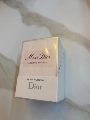 Miss Dior Blooming Bouquet parfym - Miss Dior Blooming Bouquet från Dior är en elegant parfym i en stilren, ljusrosa förpackning med silverdetaljer. Kartongen har en bild på flaskan med en söt rosett och klassisk logga. Perfekt för dig som gillar fräscha och blommiga dofter.