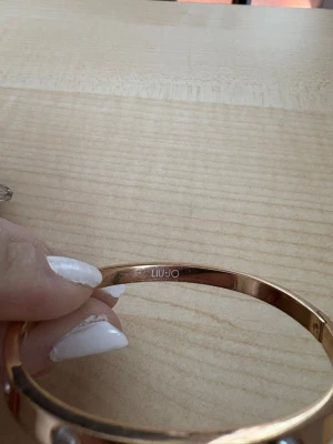 Guldigt armband från Liu Jo - Snyggt armband i guldfärgad metall från Liu Jo. Armbandet är stelt och dekorerat med flera glittrande stenar runt om som ger en exklusiv känsla. Perfekt accessoar för att lyfta din outfit och ge lite extra bling.