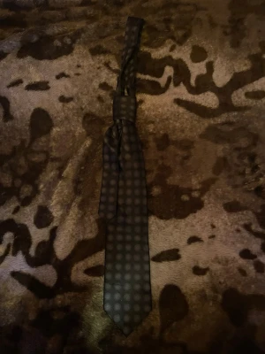 Svart slips med prickigt mönster - Snygg svart slips med diskret prickigt mönster. Slipsen har en klassisk form och är tillverkad i ett glansigt material som ger en elegant känsla. Perfekt accessoar för att lyfta din outfit med en stilren touch.