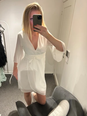 Vit klänning med knytband - Säljer en vit kort klänning med v-ringning och trekvartsärmar, perfekt nu inför studenten!! 🤍🇸🇪🥂🍾Klänningen är endast använd 1 gång på skolavslutning, jättefint skick! Band i midjan som kan knytas som man önskar, dragkedja i ryggen. Klänningen är från VILA, storlek 38.