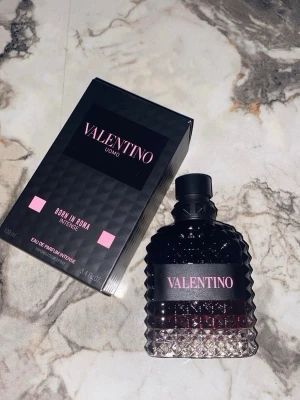 Valentino Uomo Born In Roma Intense 100ml - Valentino Uomo Born In Roma Intense är en lyxig parfym i en svart och rosa designad flaska med nitar och diamantmönster. Doften kommer i en elegant svart kartong med rosa detaljer och rymmer 100 ml Eau de Parfum Intense. Perfekt för dig som gillar exklusiva och moderna dofter.