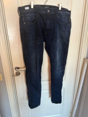 Mörkblå jeans från Replay - Snygga mörkblå jeans från Replay med klassisk femficksdesign och raka ben. Jeansen har kontrastsömmar och är gjorda i ett mjukt denimtyg som sitter skönt. Perfekta för dig som gillar en stilren och tidlös look.