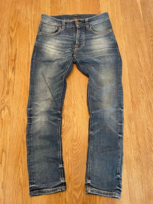 Nudie jeans - Blå Nudie jeans i modell Grim Tim med mycket slitningar. Raka ben, orangea kontrastsömmar. Perfekta för dig som gillar en avslappnad men ändå stilren stil. Inga defekter, strl W29 L30.