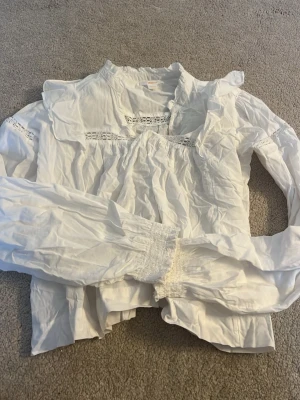 Vit blus med spetsdetaljer - Söt vit blus med långärmad design och fina spetsdetaljer vid bröstet och ärmsluten. Blusen har en bred krage och lätt puffade axlar för en romantisk look. Perfekt att styla med jeans eller kjol för en trendig outfit. Från Gina. Storlek 158/164