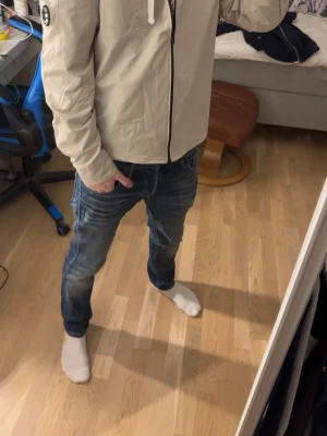 Beige jacka från C.P. Company - Säljer en beige jacka från C.P. Company med svart dragkedja och ikonisk linsdetalj på ärmen. Jackan har huva med snörning och en ficka på ärmen. Perfekt för dig som gillar stilren och modern design.