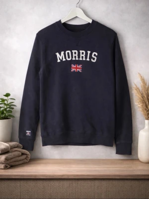 Marinblå sweatshirt från Morris - Säljer en marinblå sweatshirt från Morris med texten 'Morris' och en brittisk flagga på framsidan. Tröjan har långa ärmar och en rund halsringning. Perfekt för en avslappnad stil. Storlek Xs