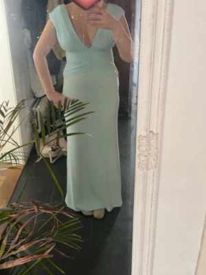 Ljusblå långklänning med v-ringning - Snygg ljusblå långklänning med djup v-ringning och cap sleeves. Klänningen har en figurnära passform och markerad midja med draperad detalj framtill. Perfekt för bal eller speciella tillfällen. Jag säljer den pga att den sitter för tajt på mig runt magen. 